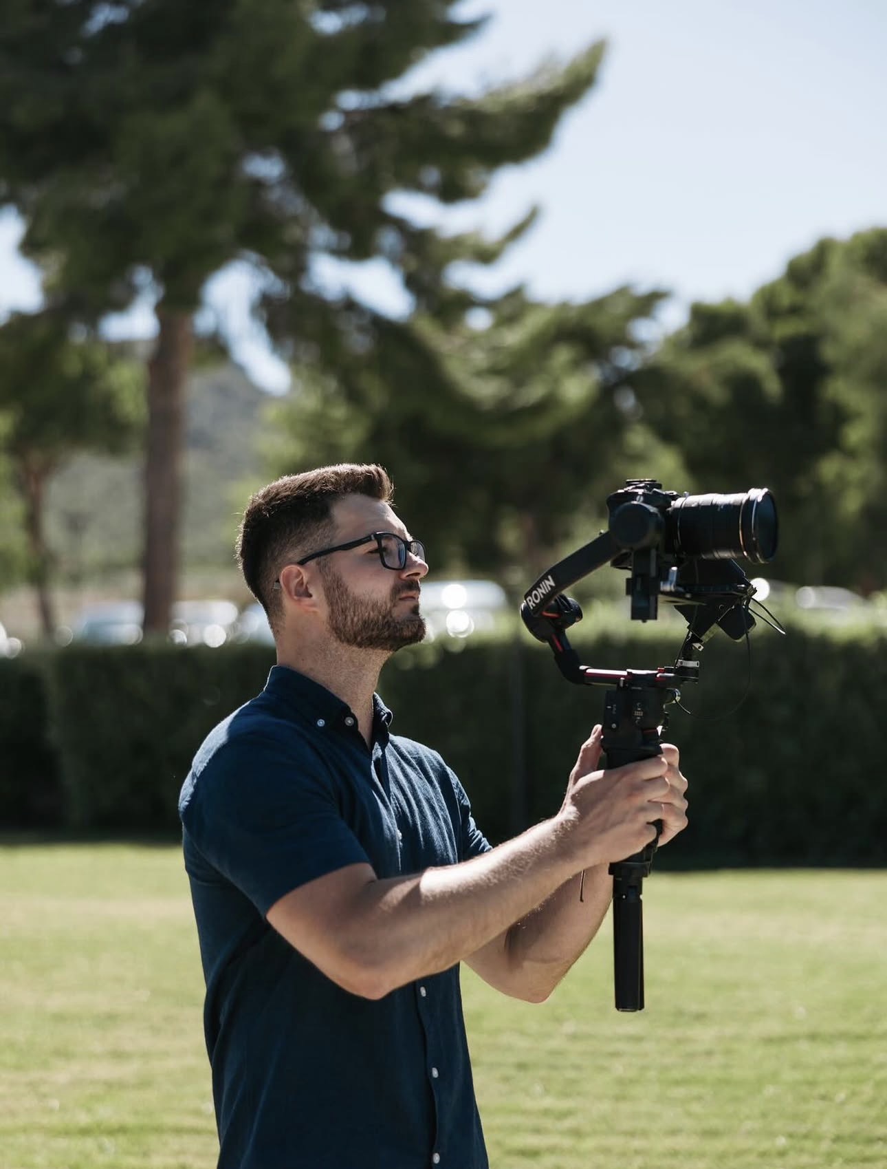 Snemalec z očali drži stabilizator s kamero na sončnem travniku